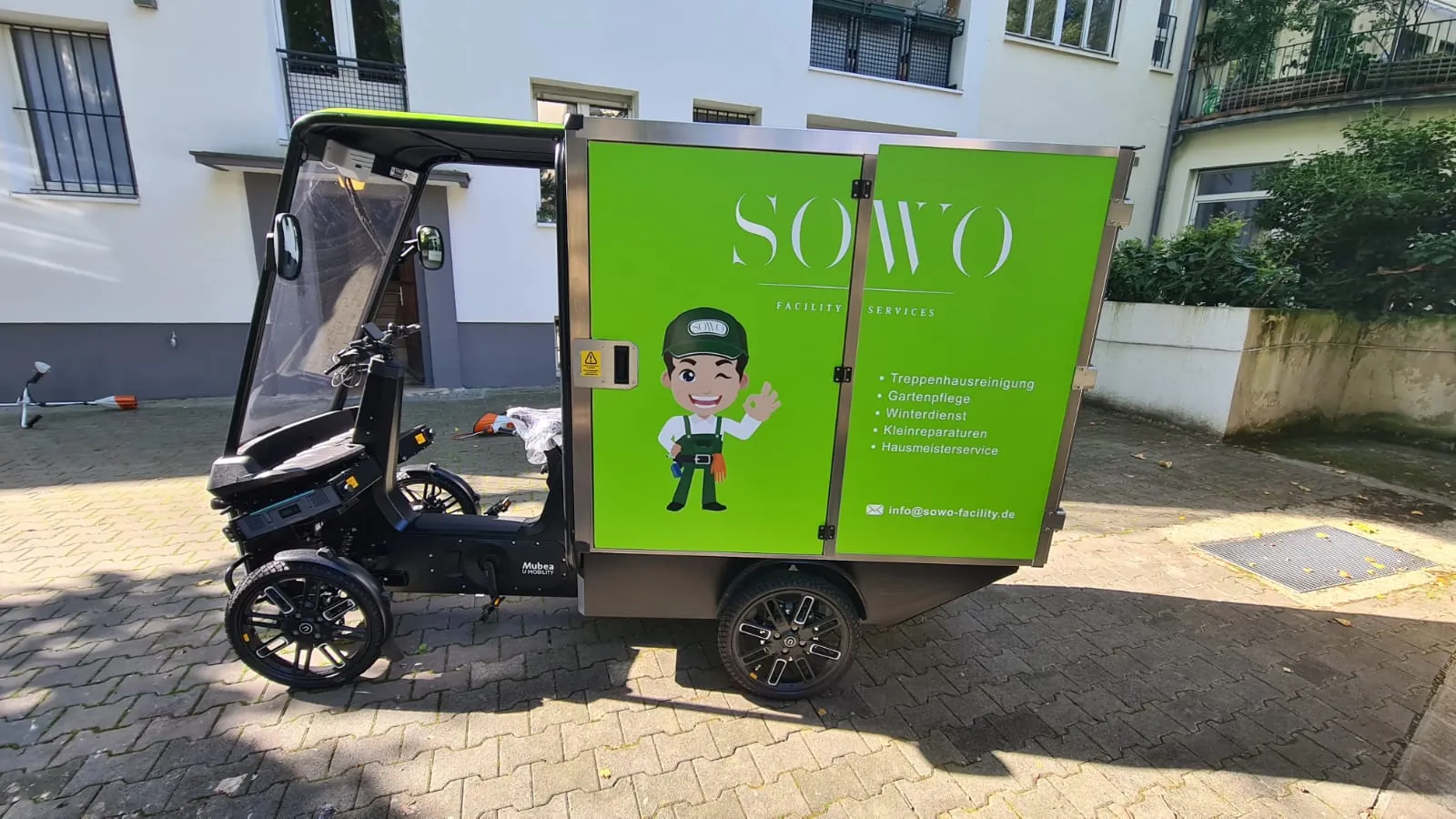 E-Lastenrad von SoWo Facility Services mit grüner Ladebox vor einem Frankfurter Mehrfamilienhaus